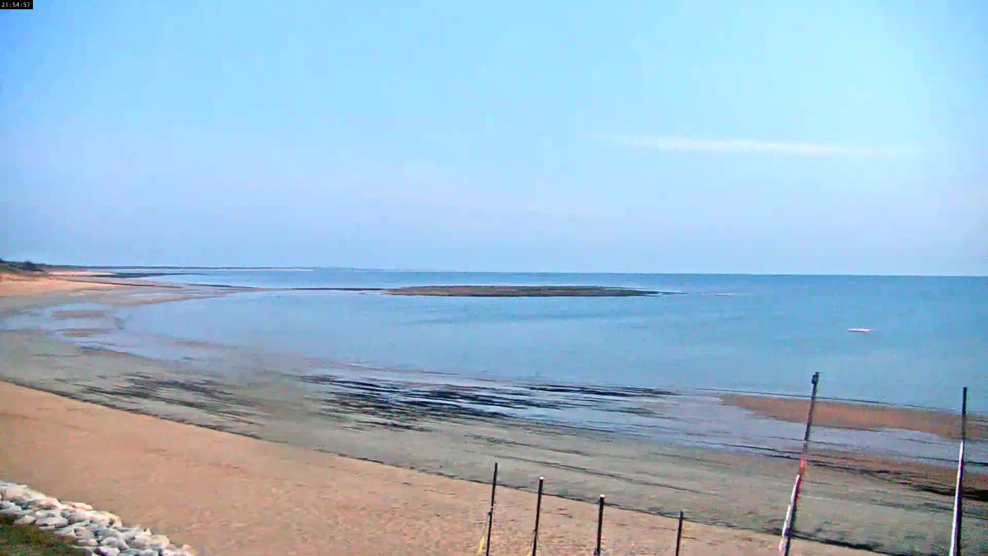 A sandy beach slopes down to calm, light-blue water under a clear, pale-blue sky.
