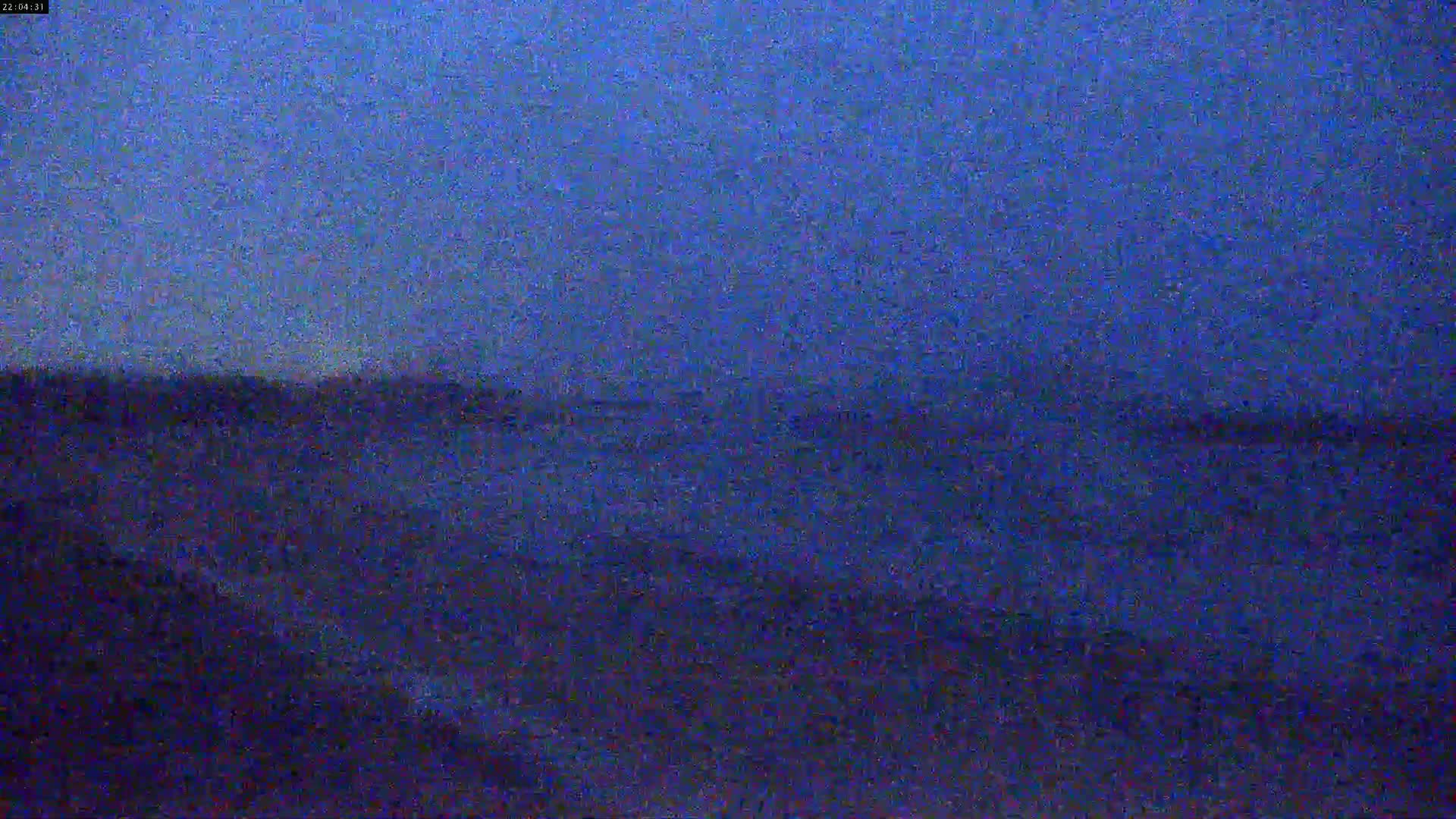 A dark blue, possibly nighttime, outdoor scene shows a blurry horizon line separating a darker landmass from a slightly lighter sky.