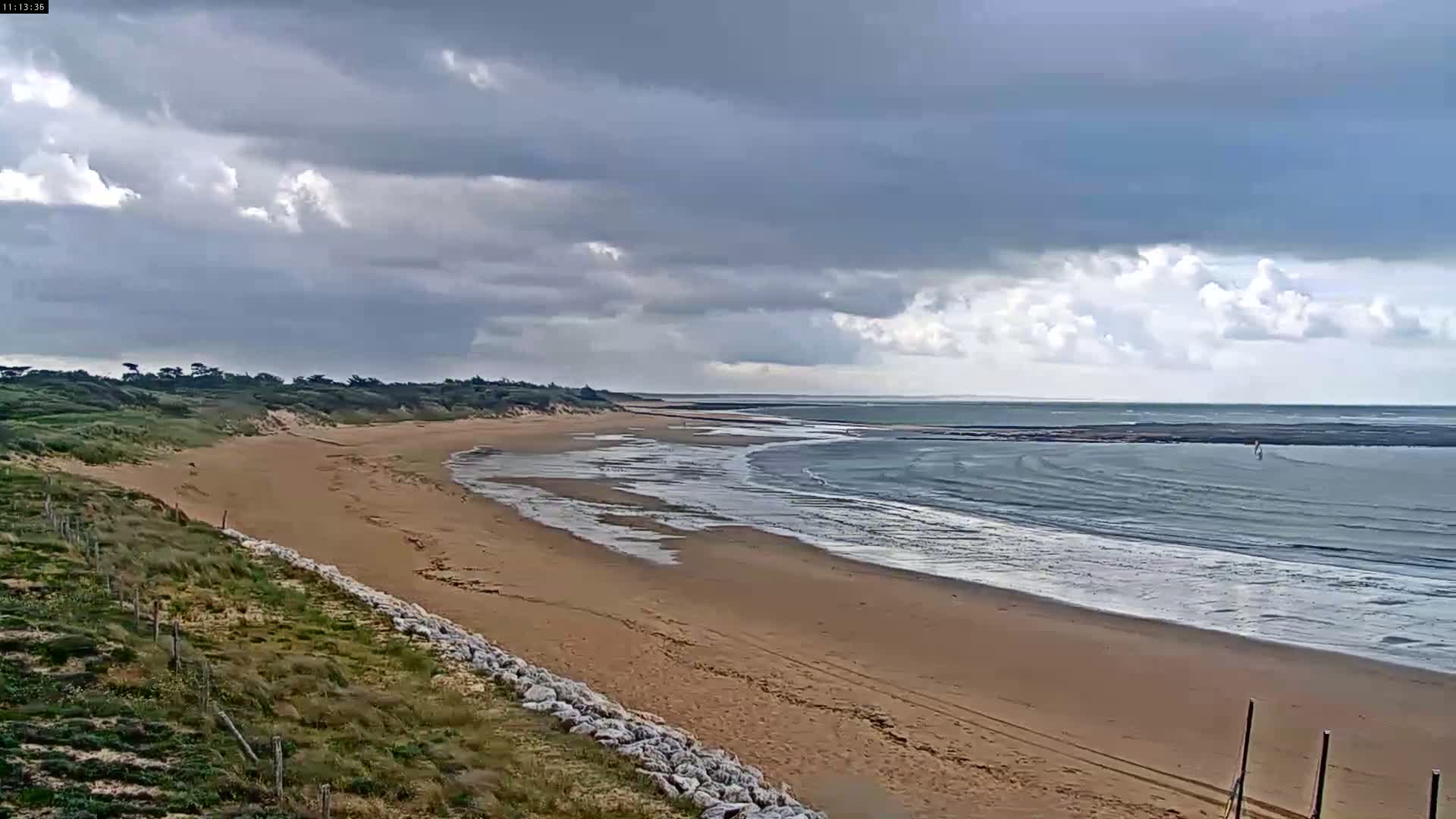 A sandy beach stretches along a calm ocean under a partly cloudy sky.