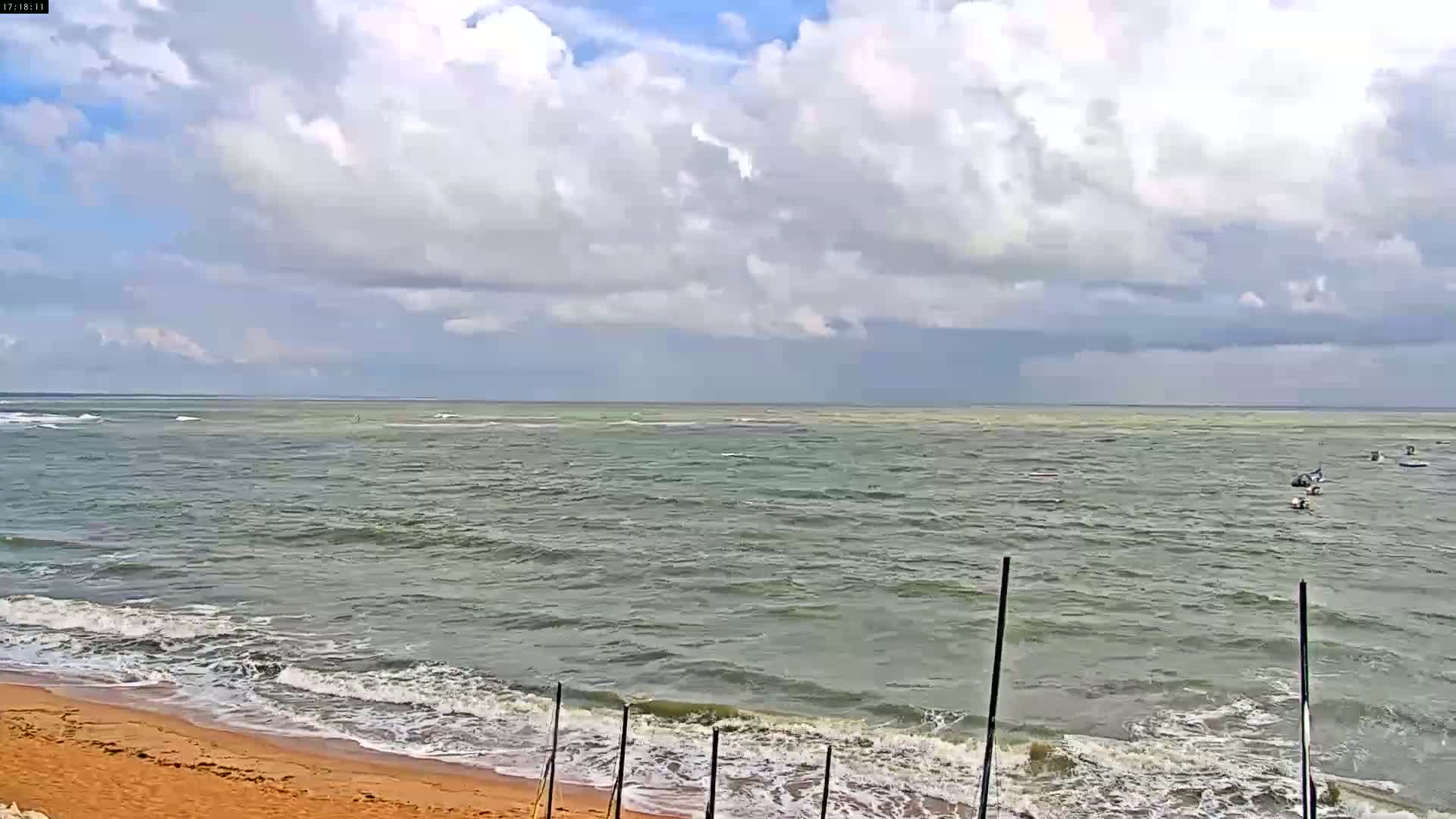A partly cloudy day shows a sandy beach with small waves lapping the shore and a choppy ocean extending to the horizon.