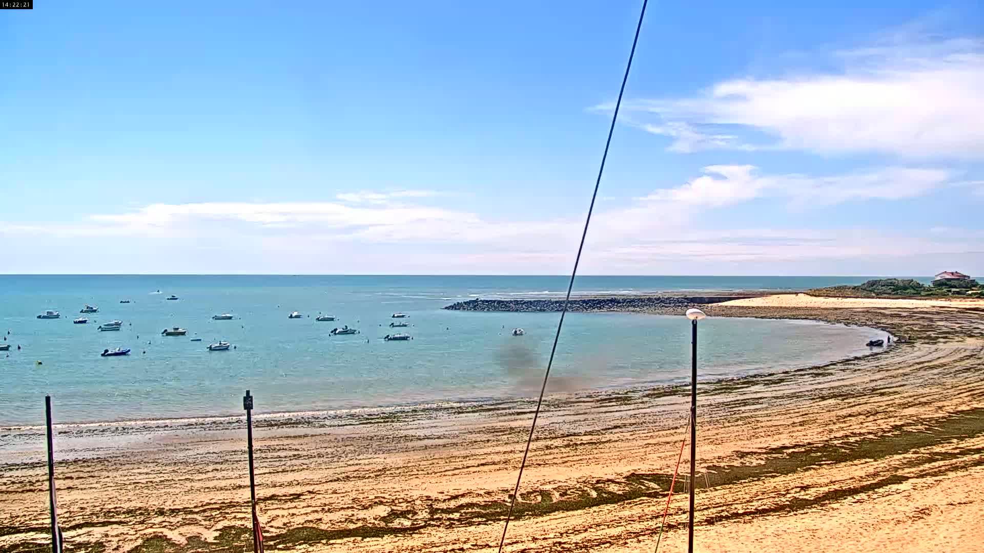 A sandy beach with several small boats in the calm, clear water under a mostly sunny sky with a few clouds.
