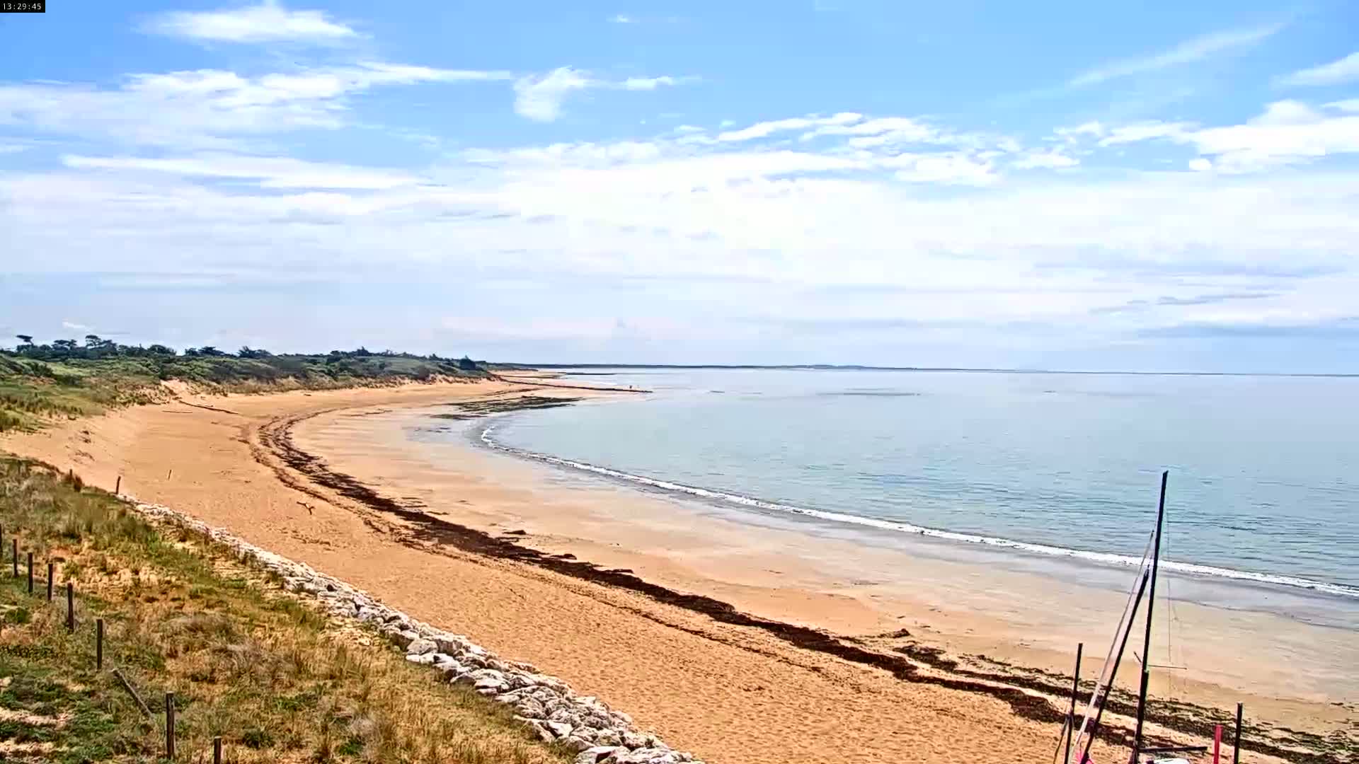 A sandy beach curves gently along a calm, light-blue ocean under a partly cloudy sky.