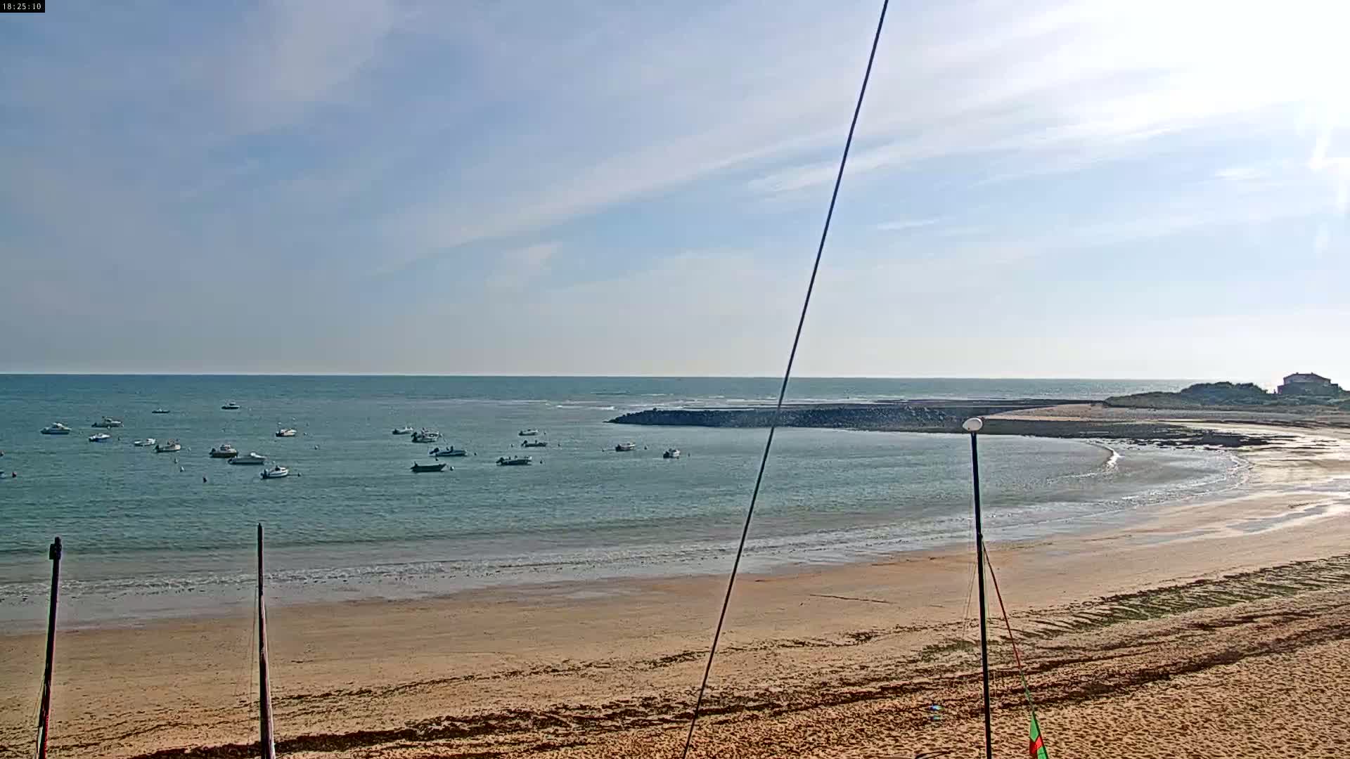 A sandy beach with calm, light-blue water, several small boats, and a partly cloudy sky.