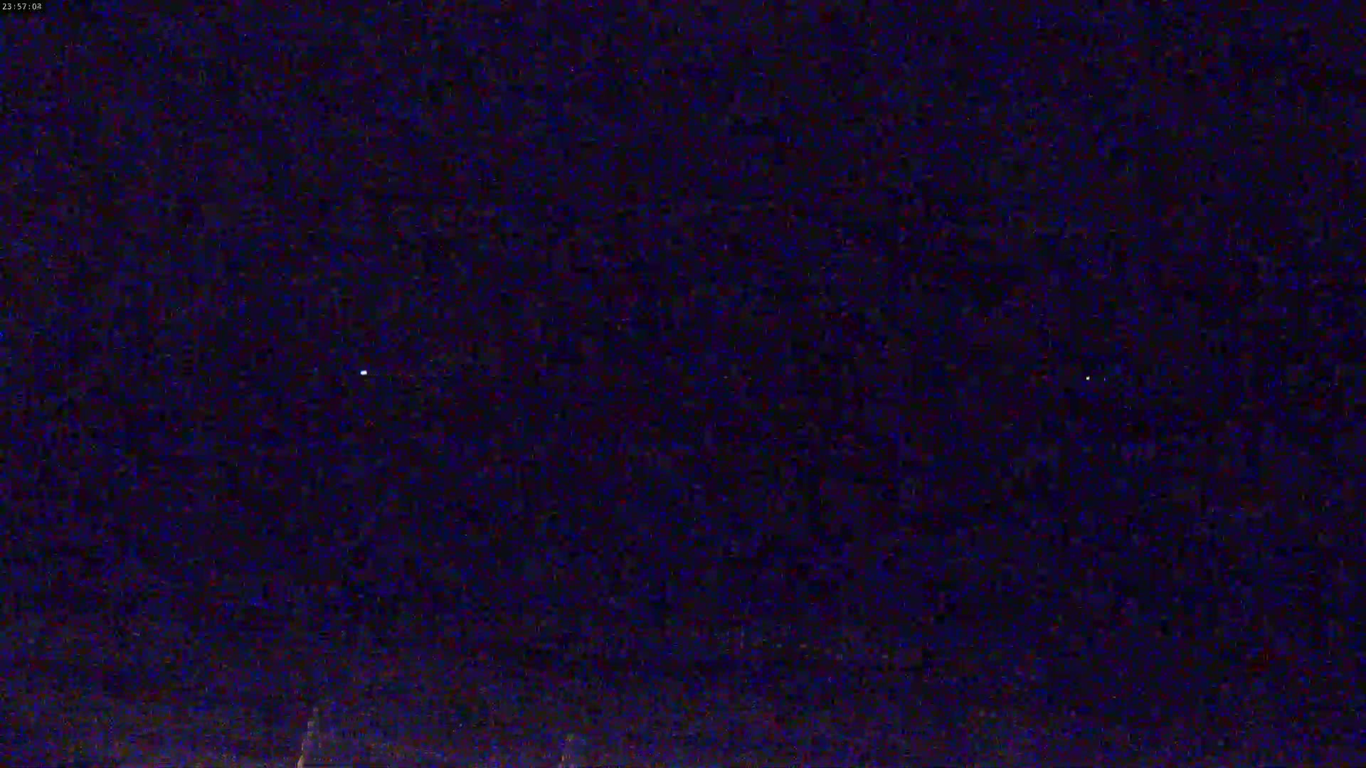 A dark, nighttime scene shows a few faint lights in the distance against a mostly clear, dark sky.