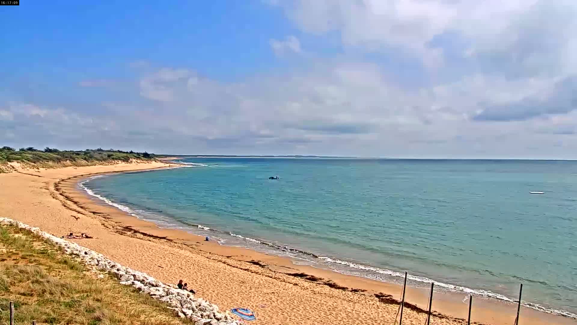 A sandy beach curves gently around a calm, teal ocean under a partly cloudy sky.