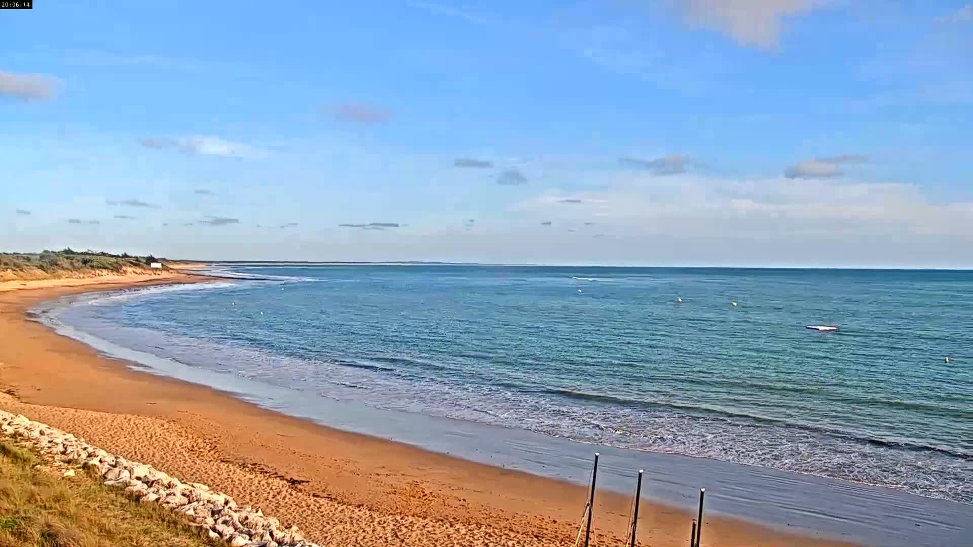 A sandy beach curves gently toward a calm, teal ocean under a mostly clear, blue sky.