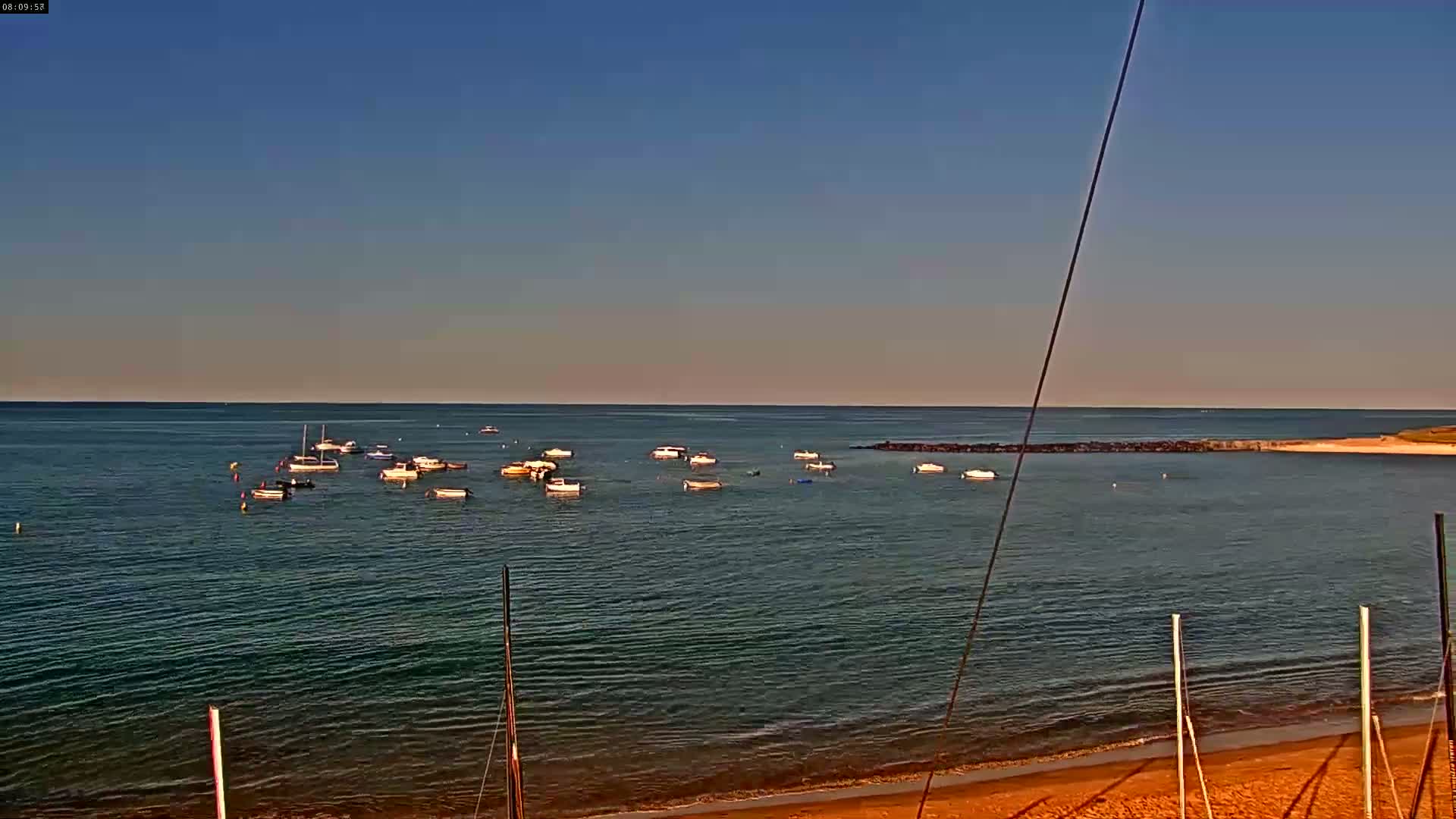Several small boats are anchored in calm, clear water near a sandy beach under a clear blue sky.
