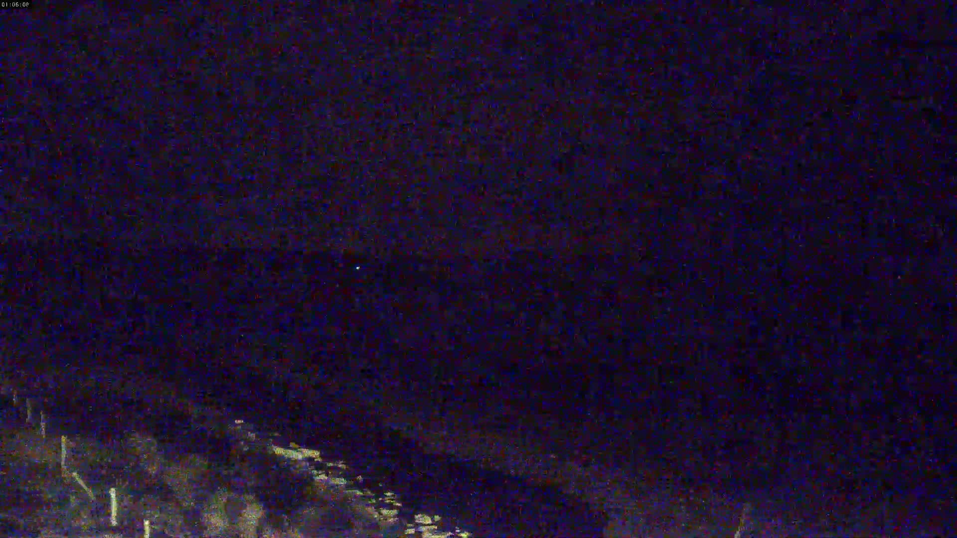 A nighttime, dark, and blurry outdoor scene shows a mostly featureless landscape with a few faintly visible objects in the bottom left corner.