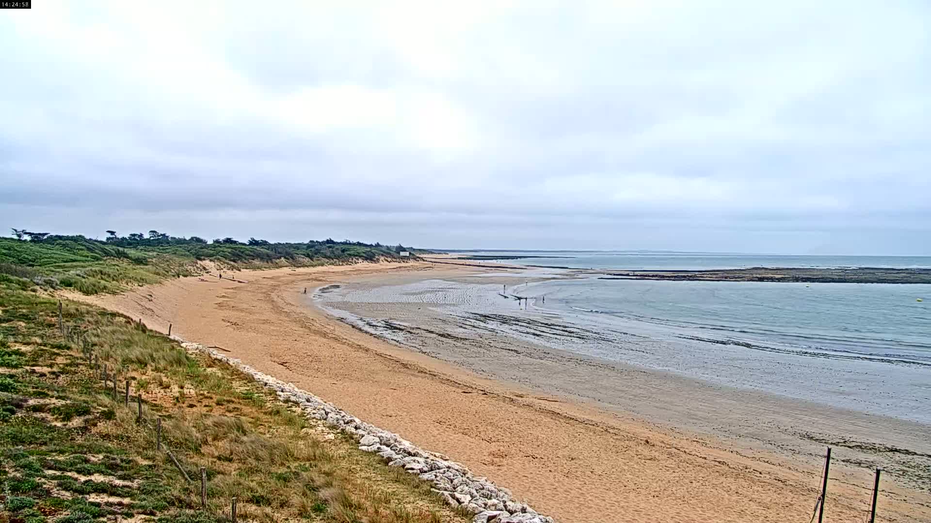 A long sandy beach stretches out to a calm sea under a cloudy sky.