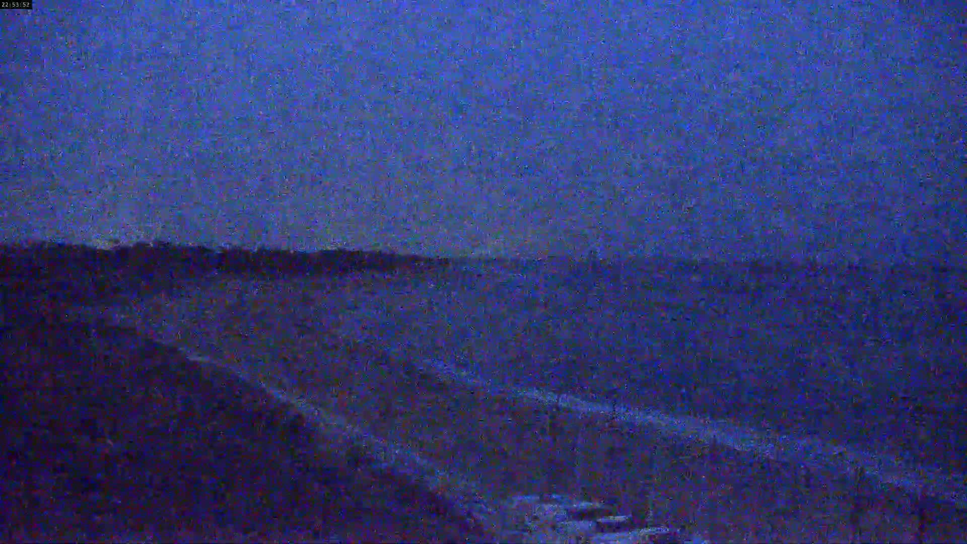 A dark, nighttime view of a flat landscape with a road or path stretching towards the horizon under a twilight sky.