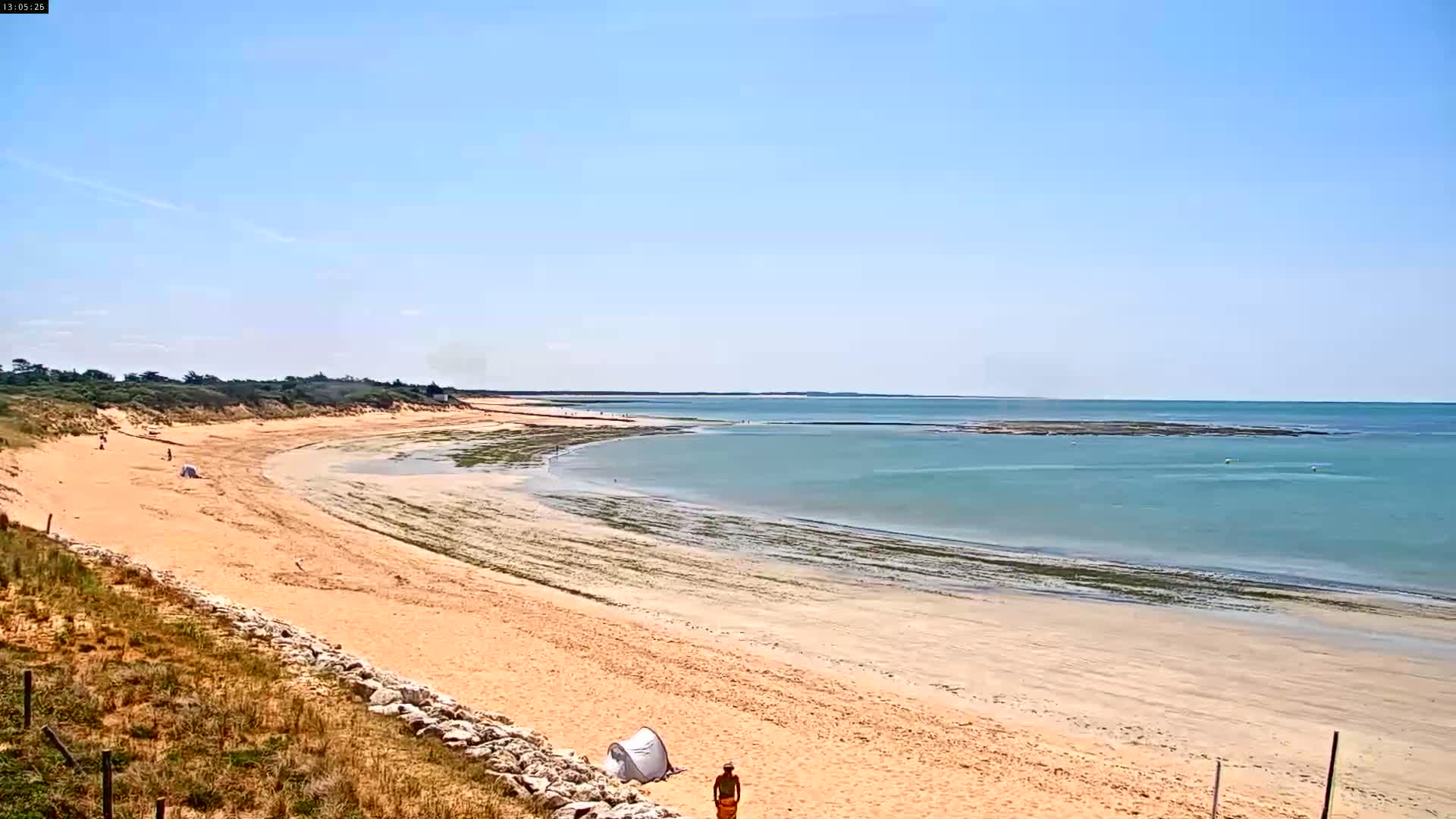 A sandy beach curves gently into a calm, light-blue sea under a clear blue sky.