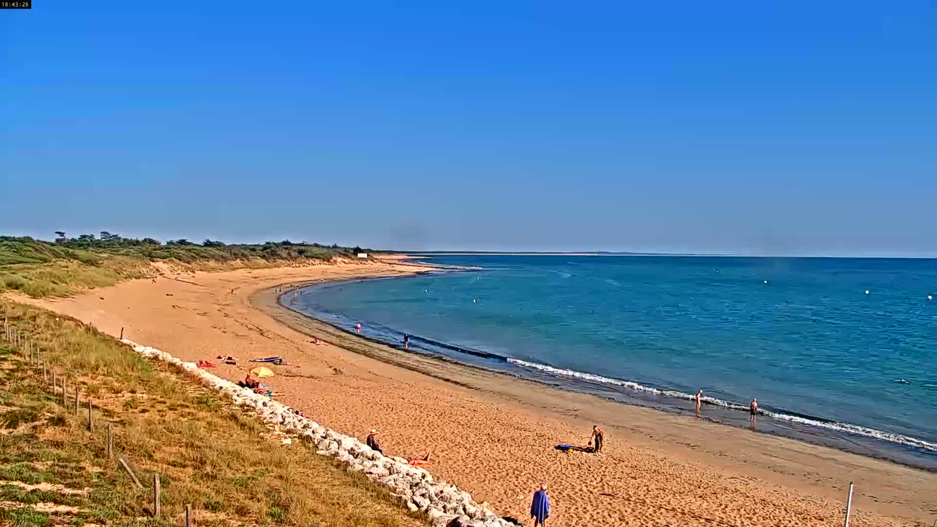 A sandy beach curves gently along a calm, turquoise ocean under a clear blue sky.