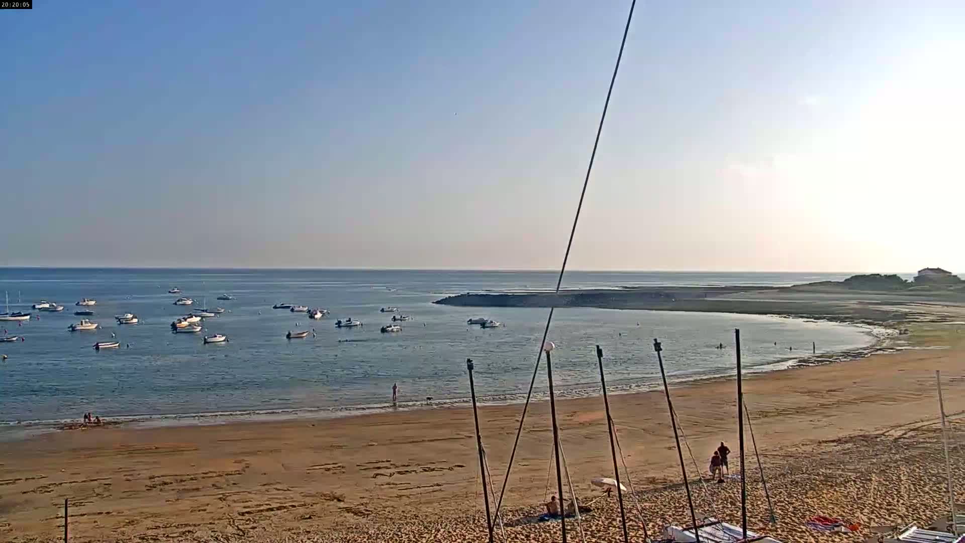 A sandy beach with numerous small boats in calm waters under a clear blue sky.