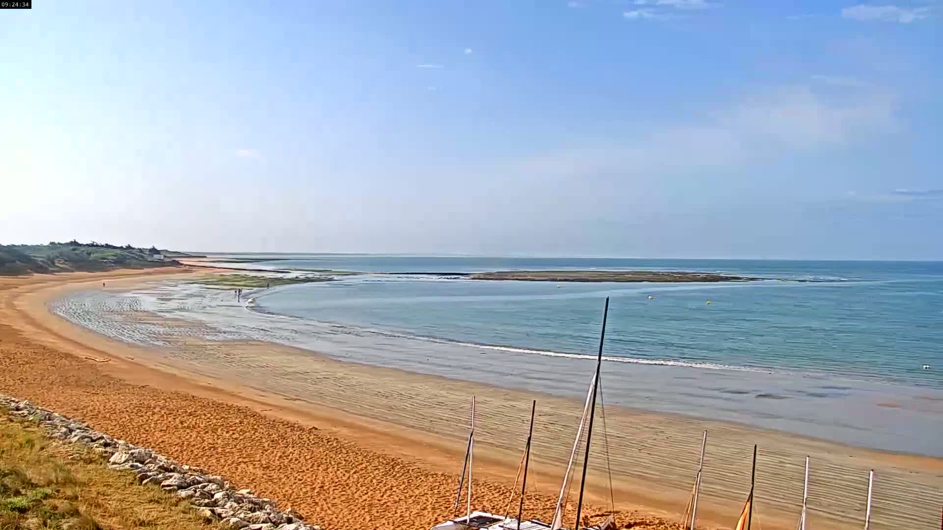 A long, sandy beach curves gently into a calm, light-blue ocean under a clear, bright sky.