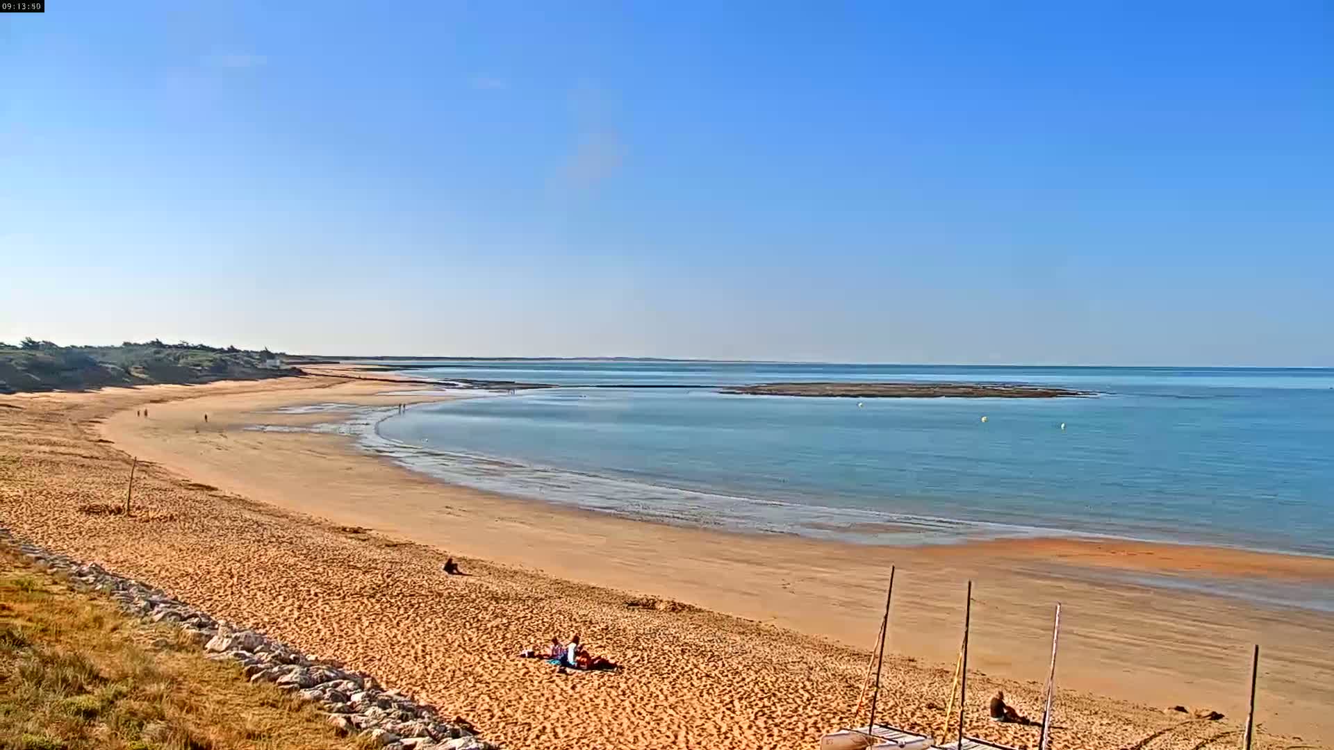 A long sandy beach stretches along a calm, light-blue ocean under a clear blue sky.