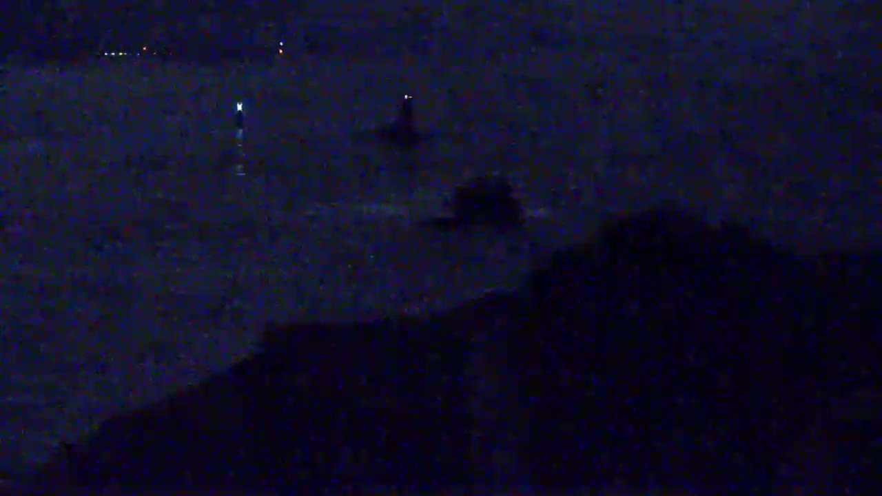 A dark, nighttime scene shows a body of water with faint lights in the distance and a dark shoreline in the foreground.