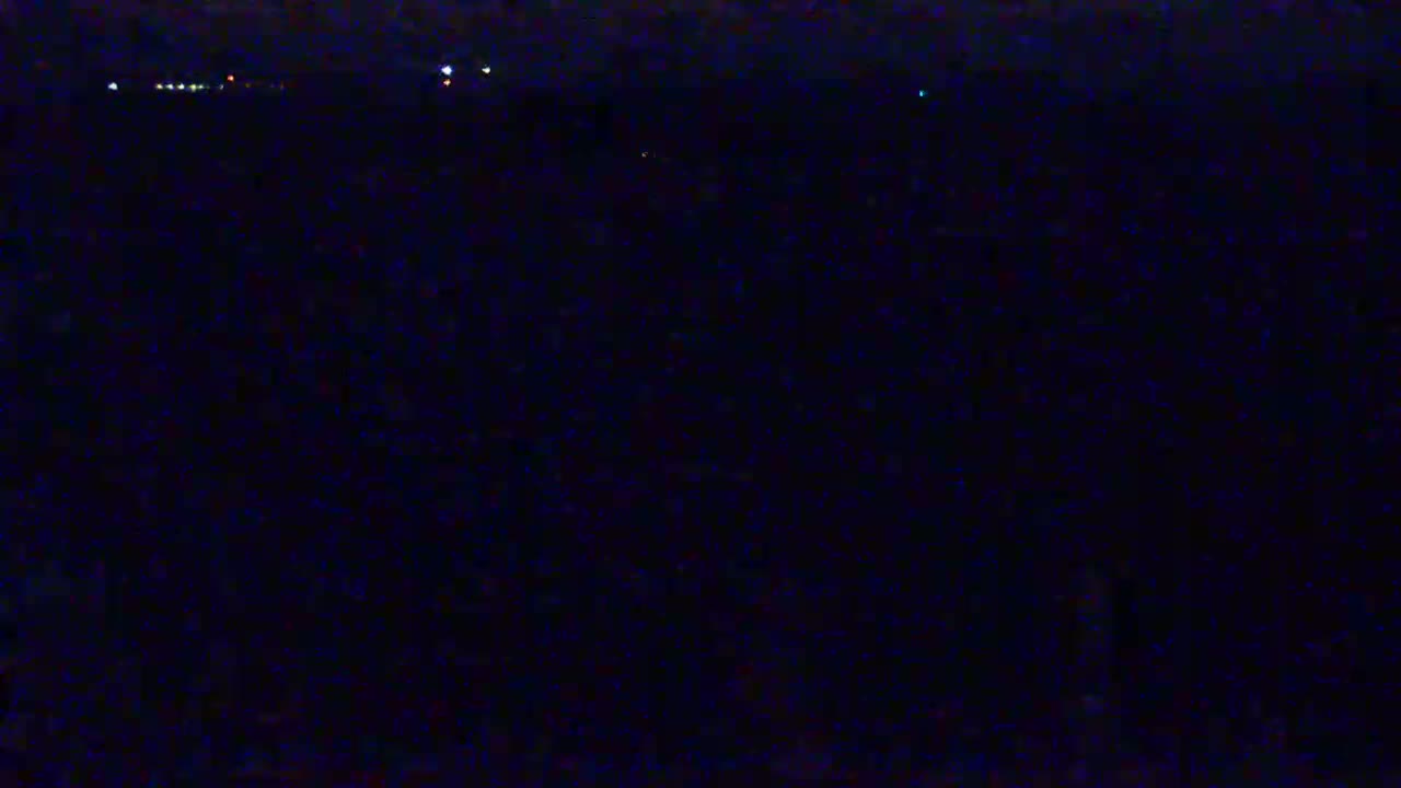 A dark, nighttime scene shows a distant line of faint lights on the horizon.