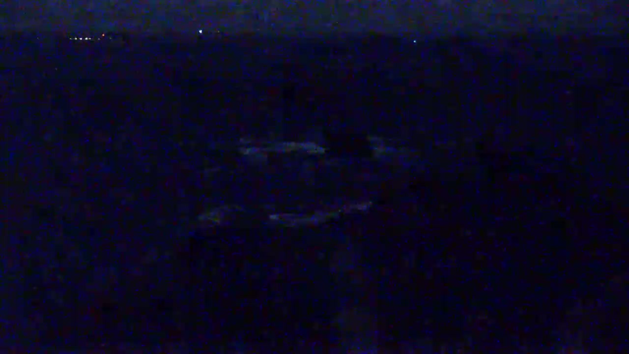 A dark, nighttime scene shows a body of water with faintly visible objects in the distance and a few lights on the horizon.