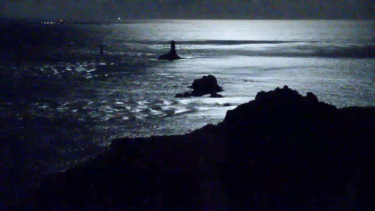 A moonlit night scene shows dark, rocky coastlines and a lighthouse extending out into a choppy sea.