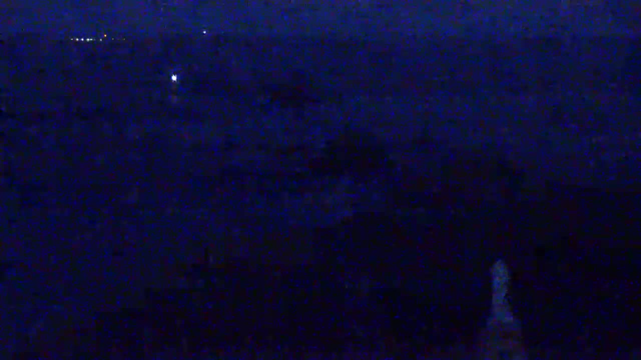 A dark, nighttime landscape is visible, with a few distant lights and a blurry, lighter area in the bottom right corner.