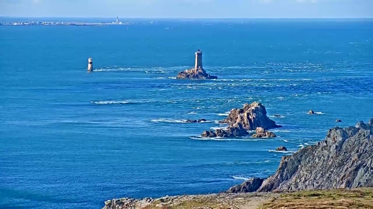 A coastal scene shows two lighthouses and rocky outcrops in a blue ocean under a clear sky.