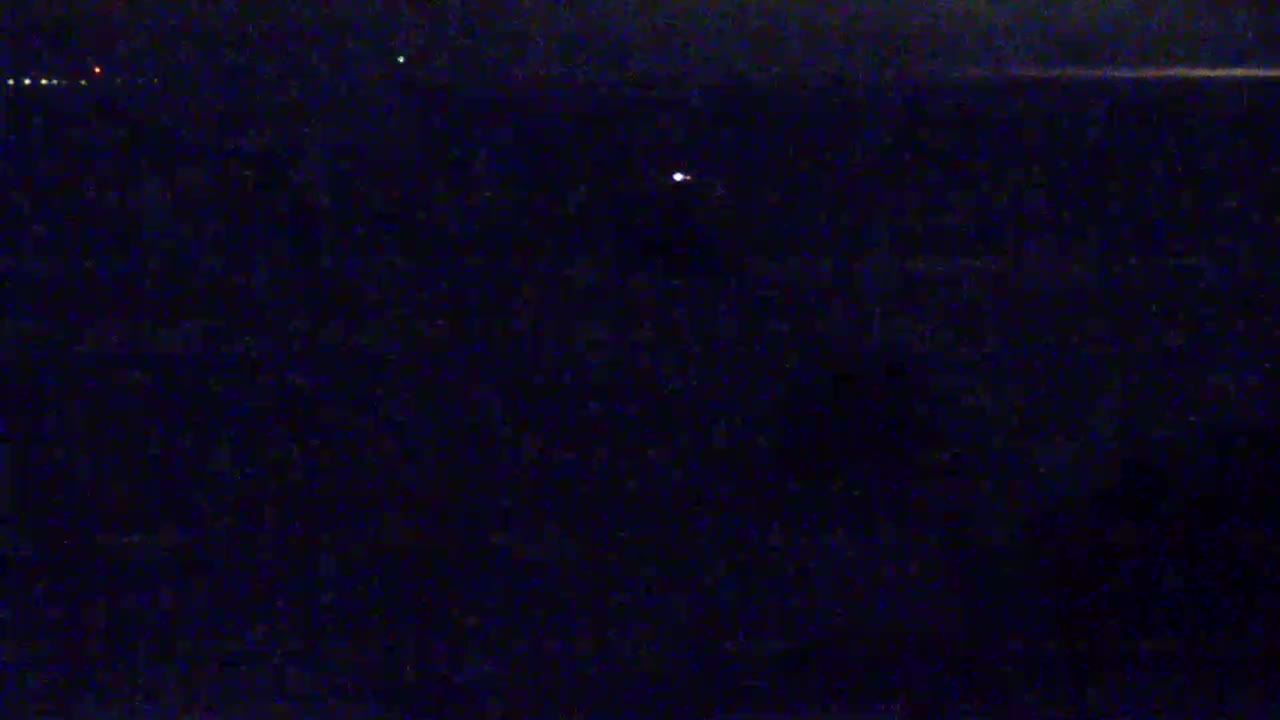 A dark, nighttime scene shows a few small lights in the distance.