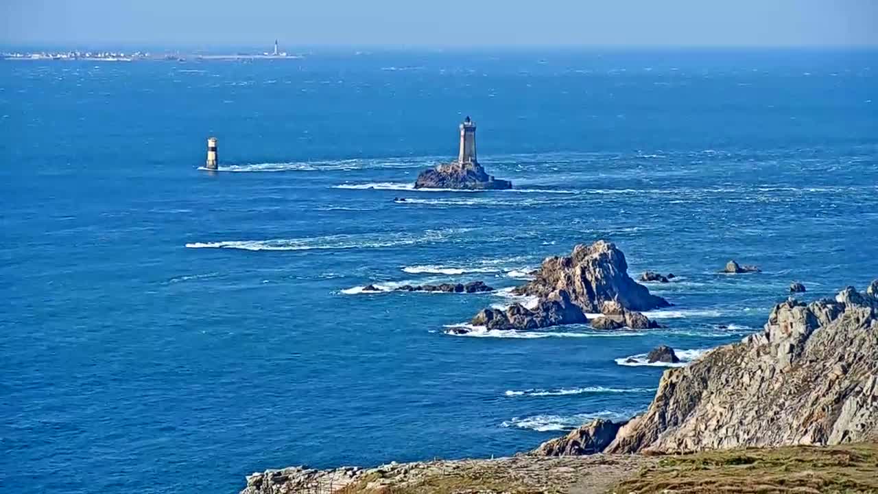A rocky coastline with two lighthouses visible on the ocean, under a clear sky with a slightly choppy sea.
