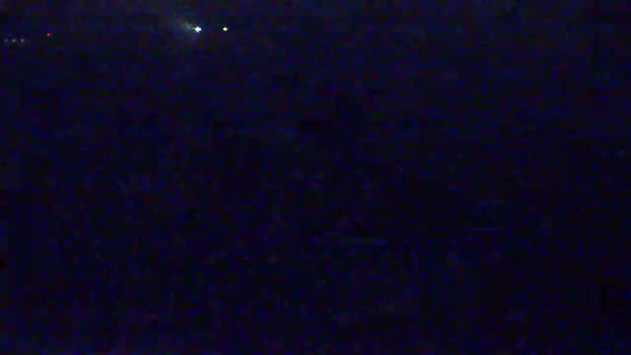A dark, nighttime scene shows a large, indistinct mass of objects, possibly a crowd, under a mostly clear sky with a few faint lights visible.