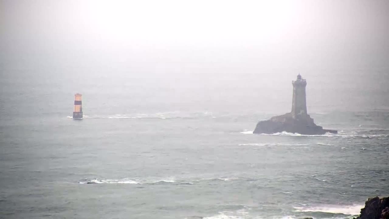 A lighthouse sits on a small, rocky island in a foggy sea, with a smaller navigational marker visible in the distance.