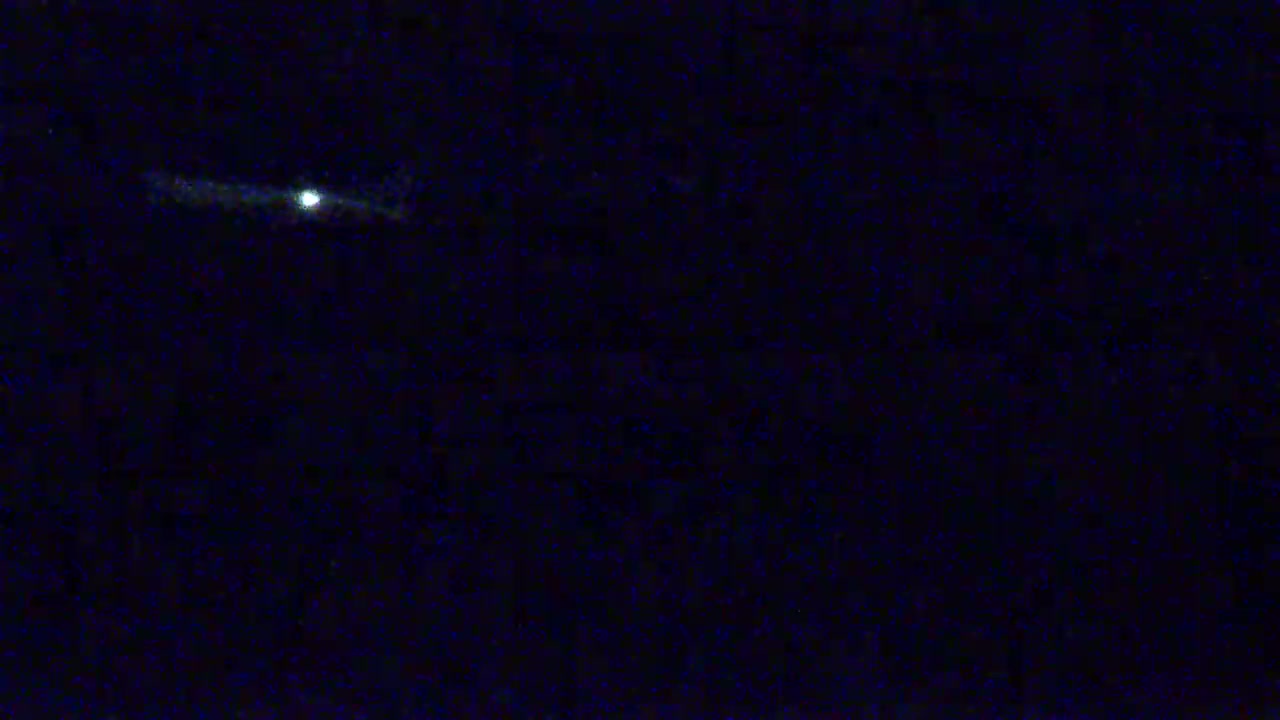 A faint, elongated streak of light, possibly a satellite or meteor, is visible against a dark, nighttime sky.