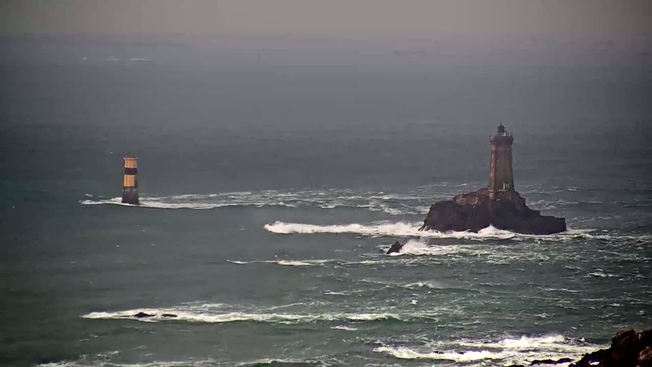Two lighthouses stand in a turbulent sea under an overcast sky.