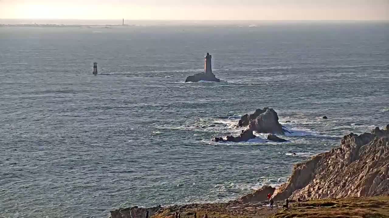 A rocky coastline with two lighthouses visible in the distance on a somewhat overcast day, with small waves crashing against the rocks.