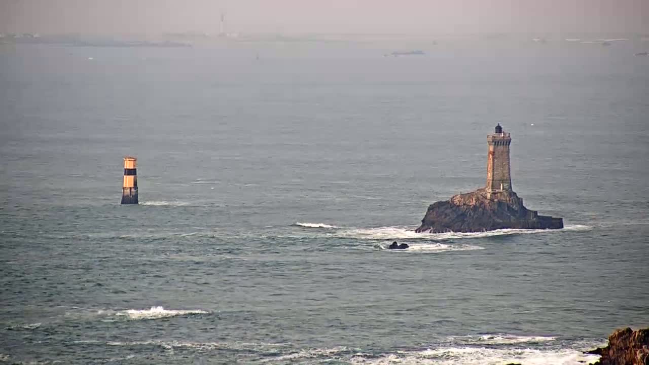 Two lighthouses stand in a gray, somewhat hazy ocean with small waves.