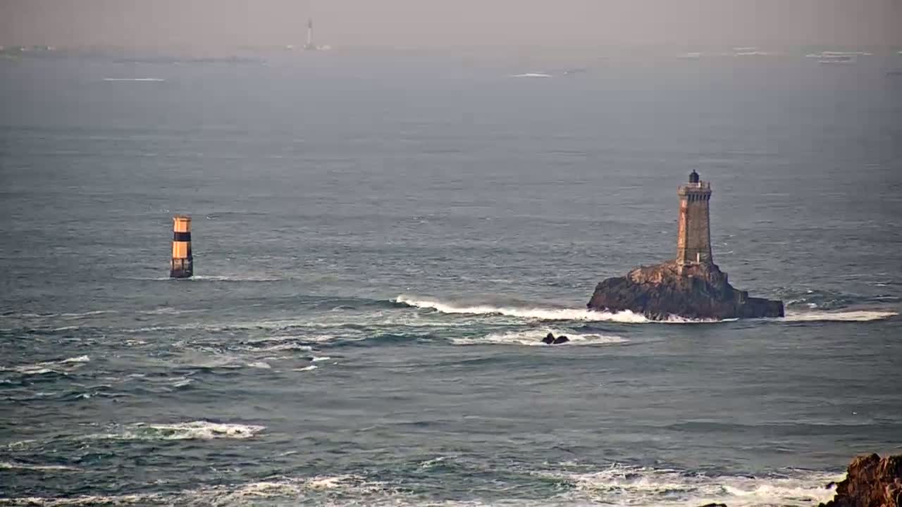 A lighthouse sits on a small, rocky island in a choppy sea, with another, smaller marker further away.