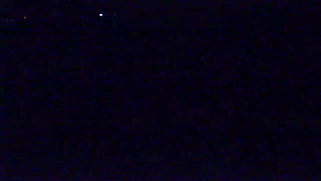 A dark, nighttime scene shows a field of indistinct, dark objects speckled with a few faint lights.