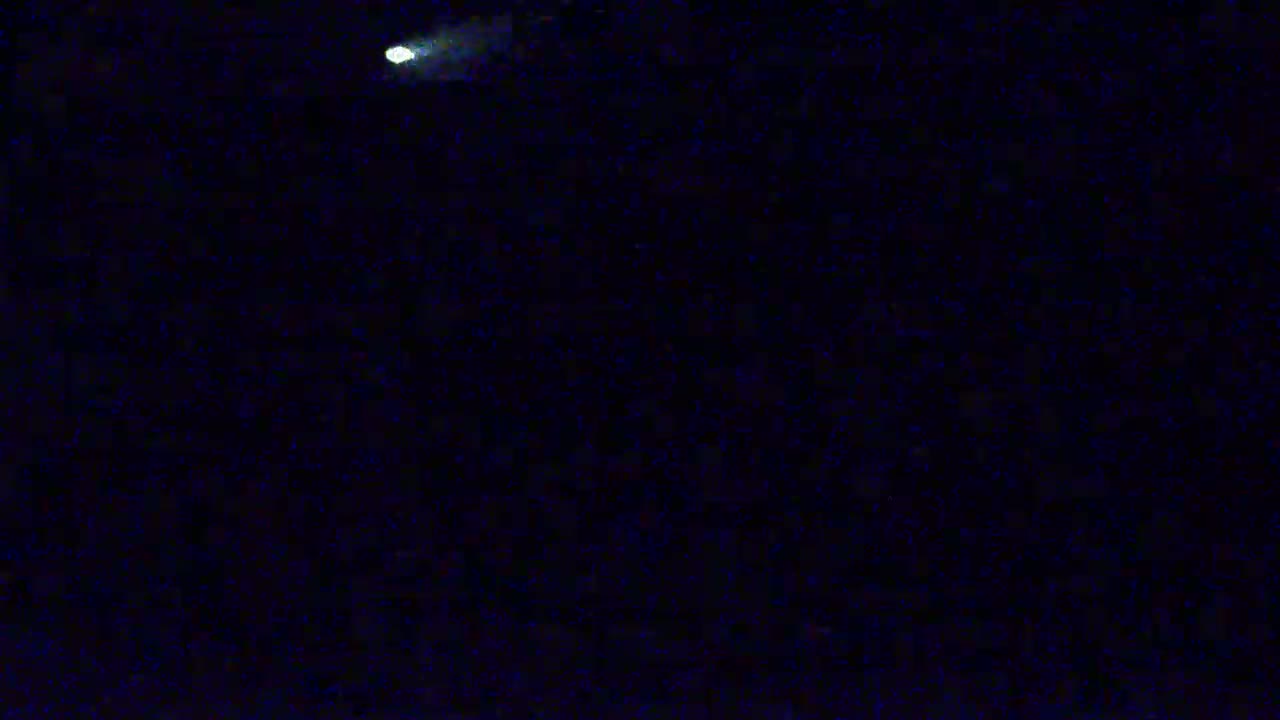 A bright light streaks across a dark, nighttime sky.