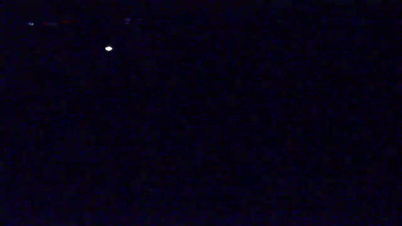 A bright, single light source is visible in a dark, nighttime sky speckled with numerous fainter lights.