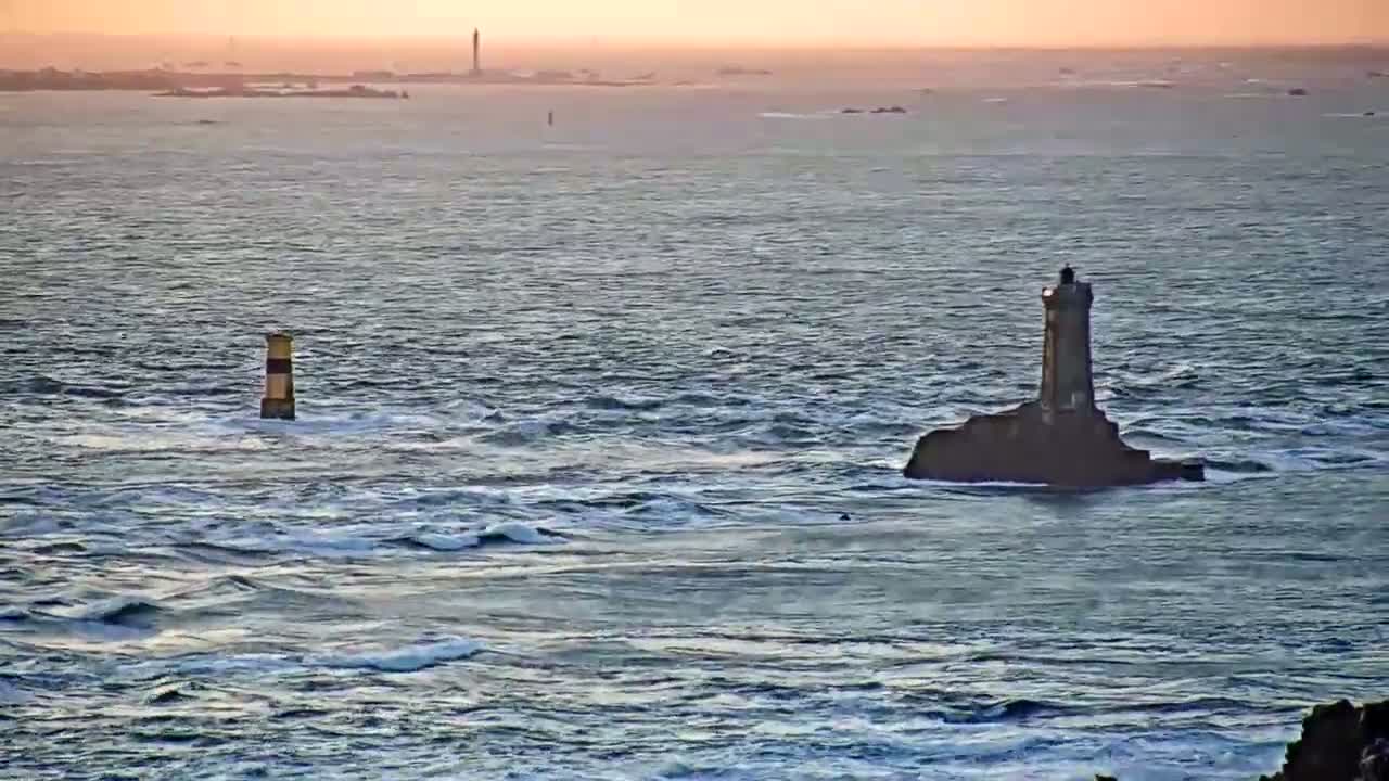 Two lighthouses stand in a choppy sea under a sunset sky.