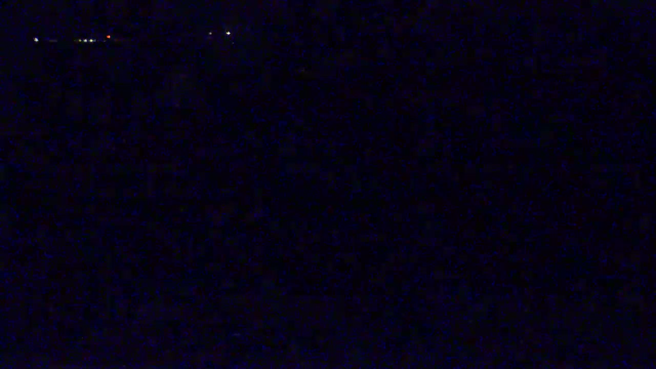 A dark, nighttime scene shows a few faint lights in the distance.