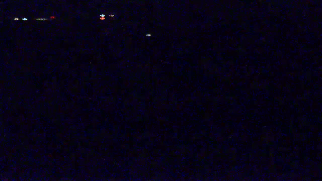 A dark, nighttime scene shows a few small, distant lights against a mostly black background.