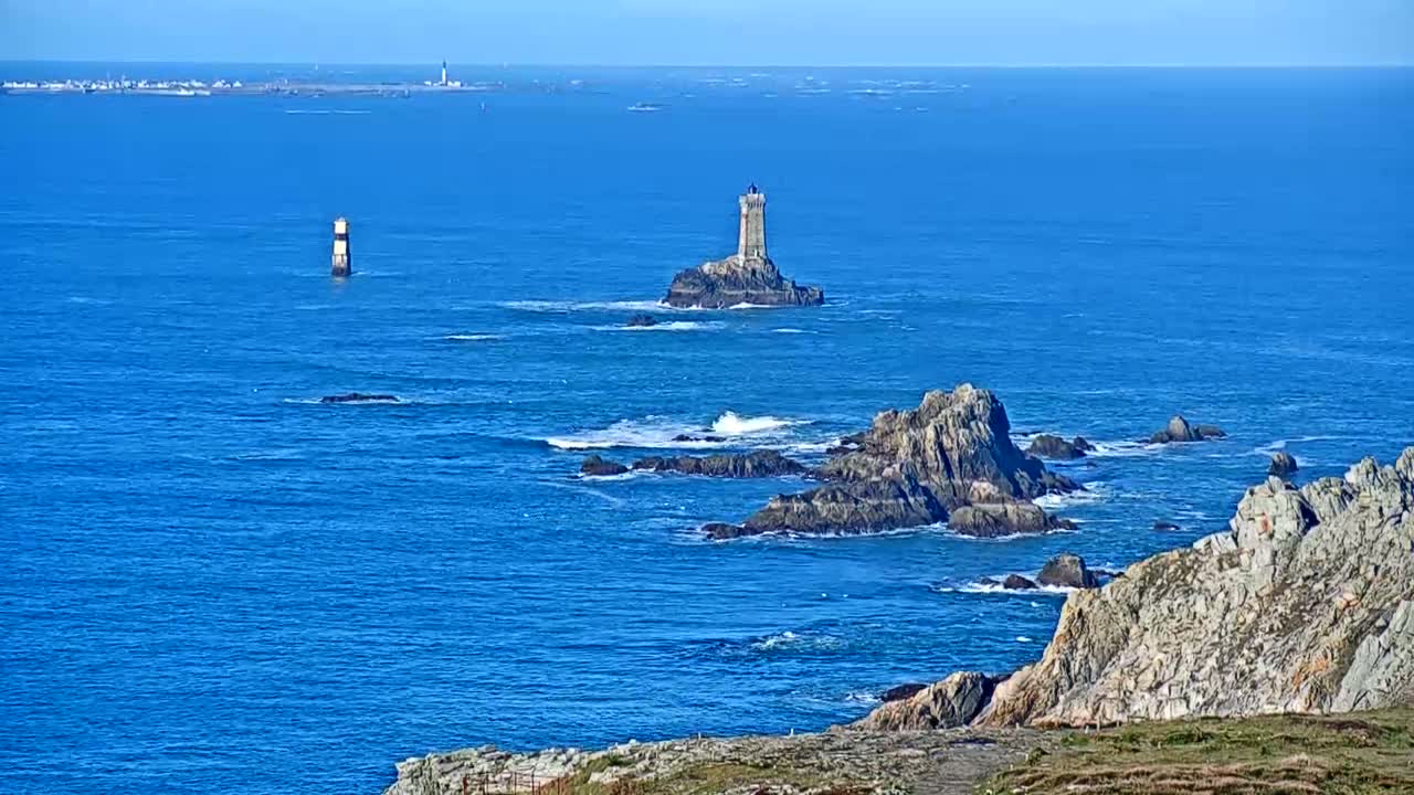 A rocky coastline with two lighthouses visible in a calm, blue ocean under a clear sky.