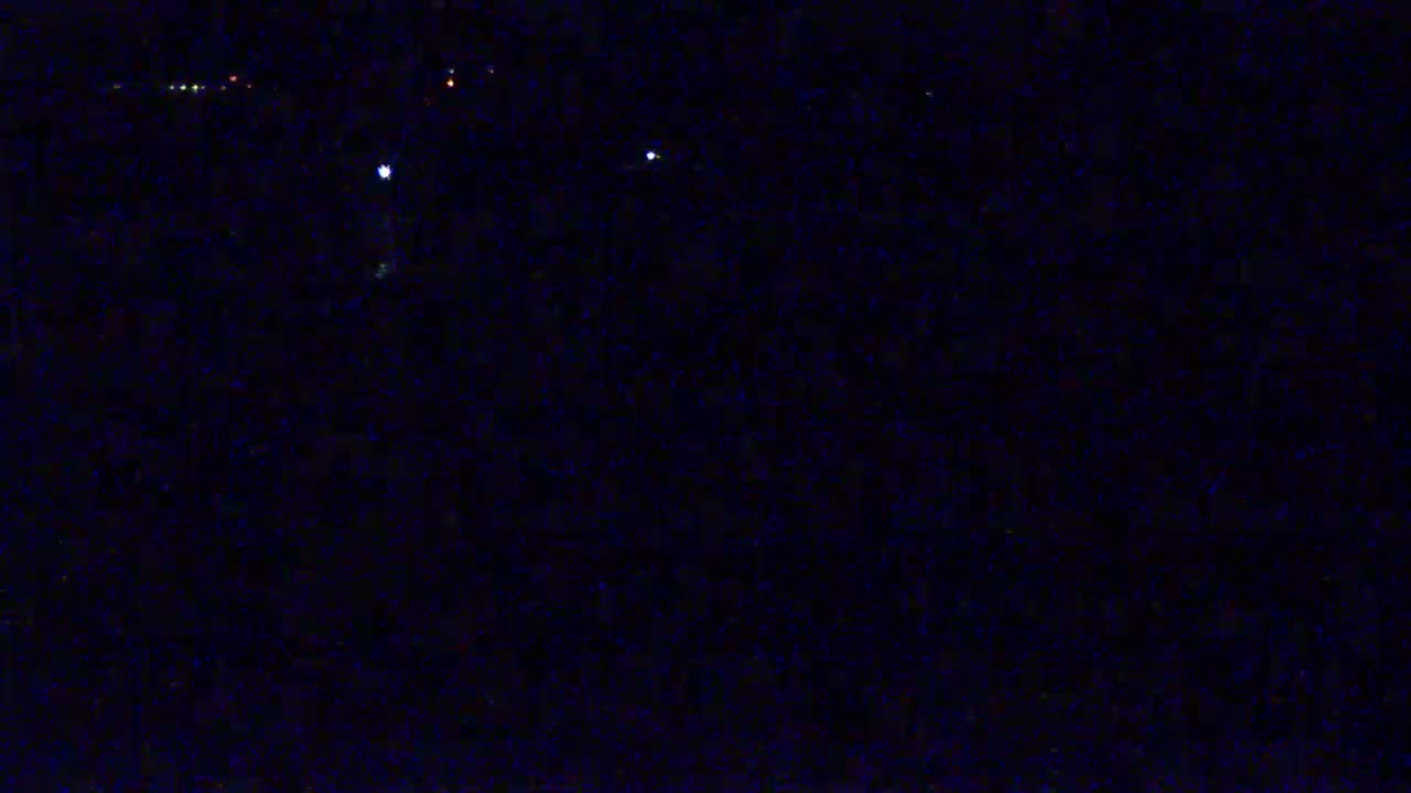 A dark, nighttime scene shows a few small, distant lights against a mostly black background.