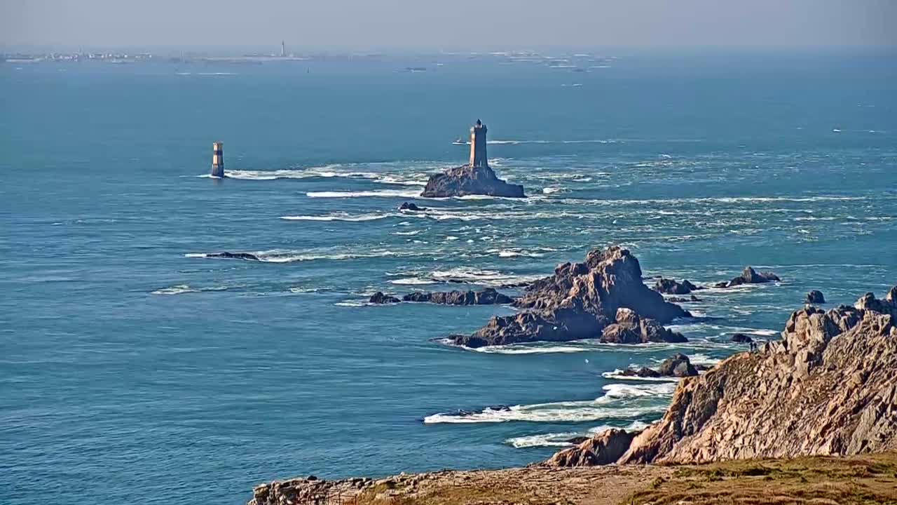 A rocky coastline with two lighthouses visible in the distance on a bright, sunny day with a slightly choppy ocean.