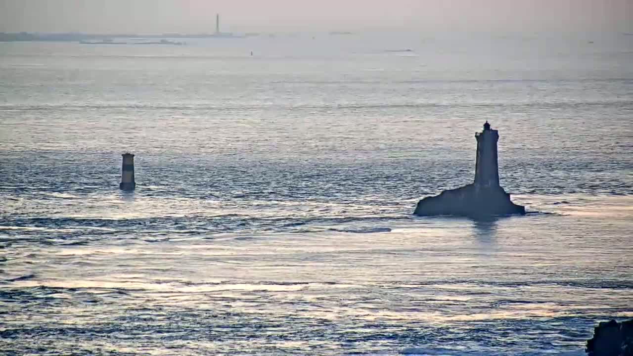 Two lighthouses stand in a calm sea under a hazy sky.