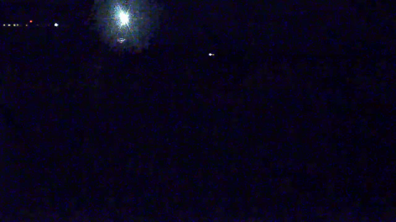A bright light dominates a dark, nighttime scene with a few faint lights visible in the distance.