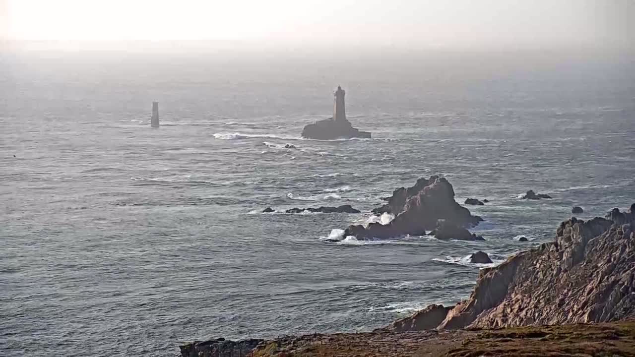 A hazy, somewhat choppy ocean scene features two lighthouses in the distance and rocky outcrops closer to the viewer.