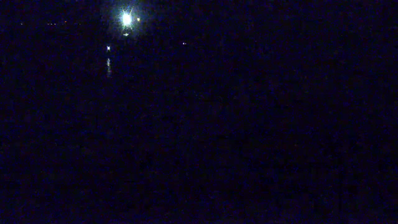 A dark, nighttime scene shows a bright light source in the distance over a dark body of water.