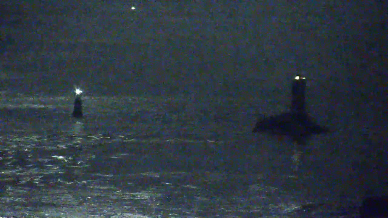 Two lighthouses are visible at night on a dark, choppy sea.