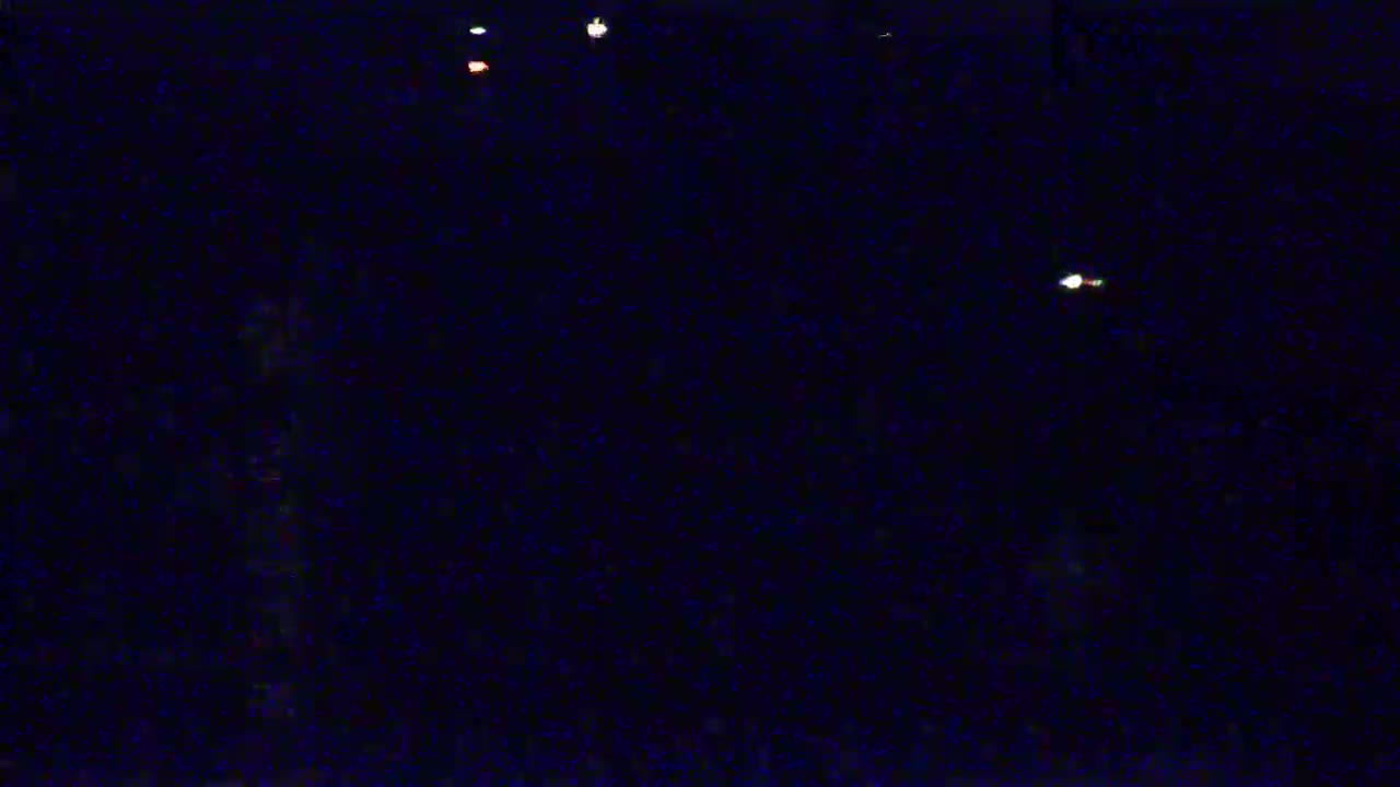 A dark, nighttime scene with a few faint lights visible in the distance.