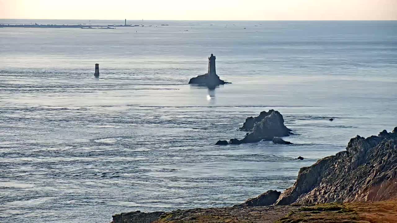 A calm, expansive ocean scene features two lighthouses on distant rocky outcrops, with dark rocky cliffs in the foreground.